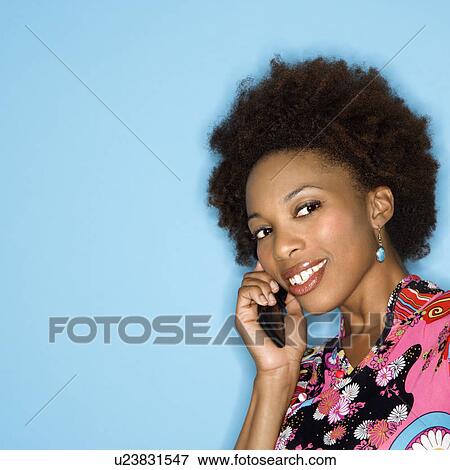 Woman with afro wearing vintage print fabric smiling holding cellphone View Large Photo Image Stock Photo - Woman with afro wearing vintage print fabric smiling holding cellphone. Fotosearch
