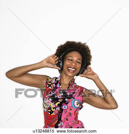Stock Photography - Woman with afro wearing vintage print fabric and listening to headphones smiling and dancing. Fotosearch