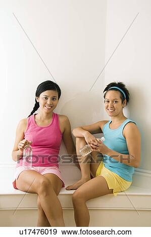 Stock Photo - Women in fitness clothes holding water bottles sitting smiling. Fotosearch