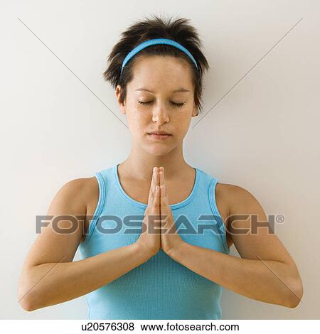 Young woman holding hands in prayer position with eyes closed meditating View Large Photo Image Stock Photo - Young woman holding hands in prayer position with eyes closed meditating. Fotosearch