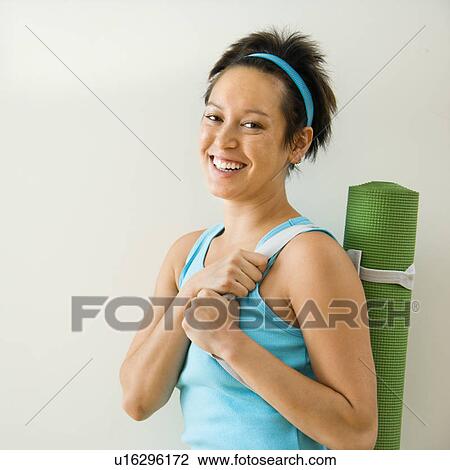 Stock Image - Young woman holding yoga mat and smiling.. Fotosearch