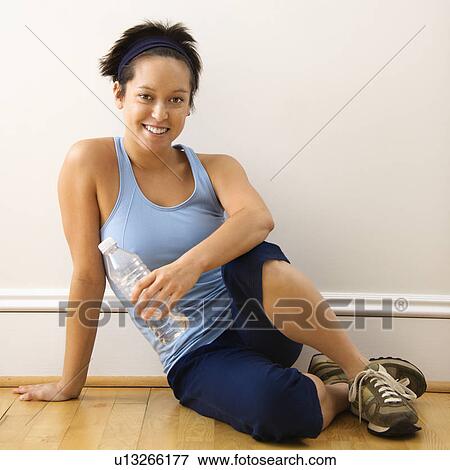 Young woman in fitness outfit sitting on floor with bottled water smiling View Large Photo Image Stock Photo - Young woman in fitness outfit sitting on floor with bottled water smiling. Fotosearch