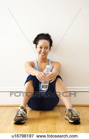 Young woman in fitness outfit sitting on floor with bottled water smiling View Large Photo Image Stock Photo - Young woman in fitness outfit sitting on floor with bottled water smiling. Fotosearch