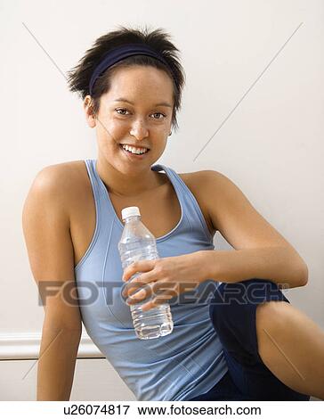 Young woman in fitness outfit sitting on floor with bottled water smiling View Large Photo Image Stock Photo - Young woman in fitness outfit sitting on floor with bottled water smiling. Fotosearch