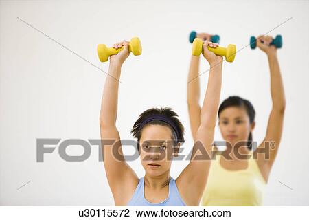 Stock Image - Young women at gym lifting hand weights. Fotosearch