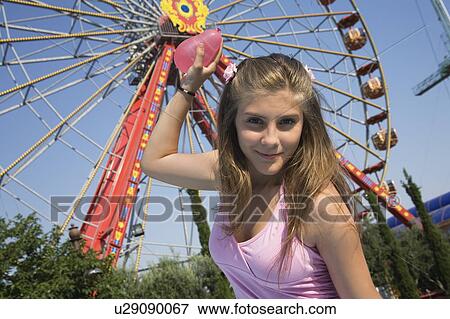 Stock Photo - Female teenager holding water balloon at Ferris wheel in amusement park. Fotosearch