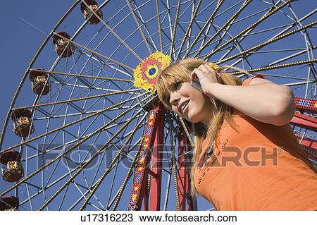 Stock Image - Female teenager on cell phone at Ferris wheel in amusement park. Fotosearch