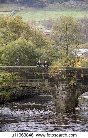 Stock Photograph - People feeding the ducks from a bridge. Hebden Bridge, Yorkshire Pennines, UK.. Fotosearch