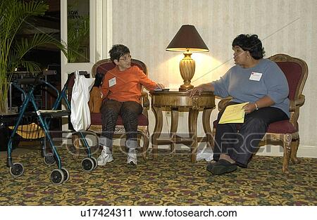 Stock Image - Two women taking a break during a conference. One woman has a disability and uses a walker for mobility assistance.. Fotosearch