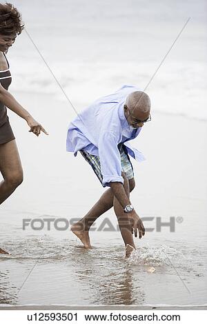 Stock Image - Couple reaching for stone on beach. Fotosearch