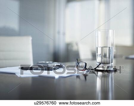 Stock Image - Eyeglasses, cell phone and pen on documents near drinking glass. Fotosearch