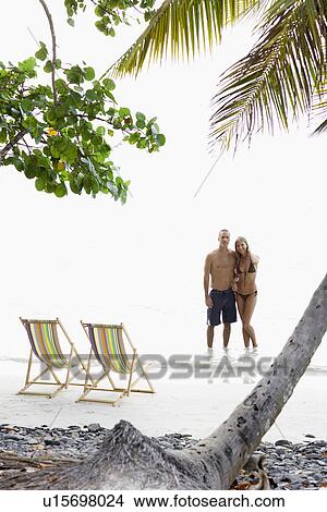 Mid adult couple standing near lounge chairs on beach View Large Photo Image Picture - Mid adult couple standing near lounge chairs on beach. Fotosearch