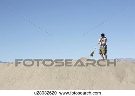 Stock Image - Woman sweeping on sand dune. Fotosearch