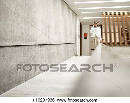 Stock Photograph - Businesswoman talking on phone by concrete wall. Fotosearch