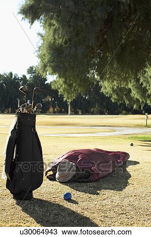 Stock Image - Man sleeping by golf bag. Fotosearch