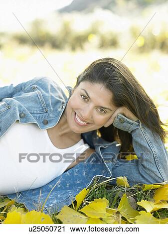 Stock Image - Mid adult woman lying on autumn leaves, portrait. Fotosearch