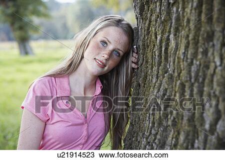 Stock Image - Teenage girl leaning on tree trunk (portrait). Fotosearch