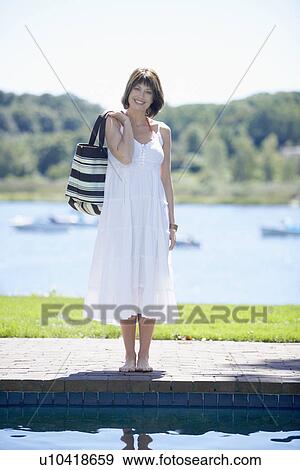 Stock Photo - Woman in white dress standing by pool. Fotosearch