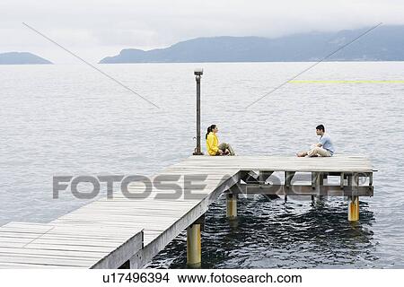 Young couple sitting on jetty View Large Photo Image Picture - Young couple sitting on jetty. Fotosearch