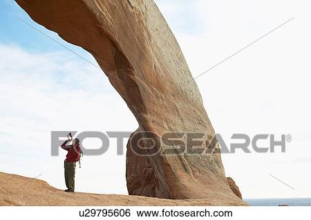 Stock Photograph - Young man playing bugle under arched rock. Fotosearch