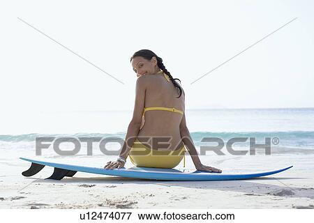 Stock Photo - Young woman sitting on surfboard, St. John, US Virgin Islands, USA. Fotosearch