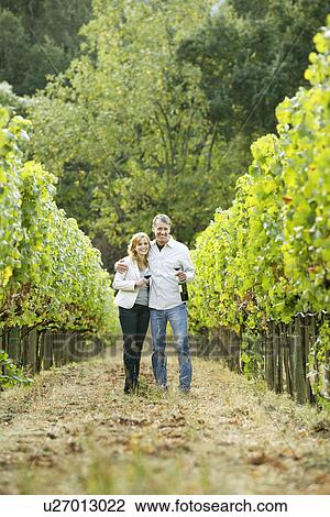 Stock Image - Couple standing in vineyard (portrait), Napa Valley, California, USA. Fotosearch