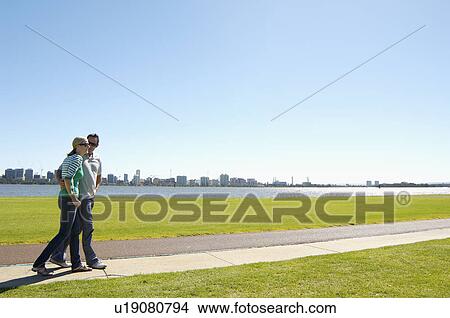Picture - Mature couple walking by river with city in background, Perth, Australia. Fotosearch