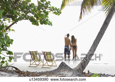 Stock Image - Mid adult couple standing on beach and looking at view, St. John, US Virgin Islands, USA. Fotosearch