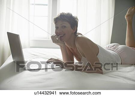 Mid adult woman using laptop on bed View Large Photo Image Stock Image - Mid adult woman using laptop on bed. Fotosearch