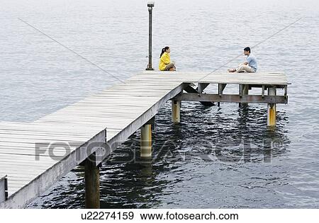 Young couple sitting on jetty View Large Photo Image Stock Photo - Young couple sitting on jetty. Fotosearch