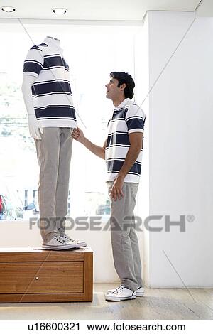 Stock Image - Young man and mannequin with identical clothes. Fotosearch