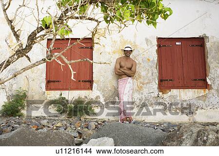 Young man in sarong and hat standing by old house View Large Photo Image Picture - Young man in sarong and hat standing by old house. Fotosearch