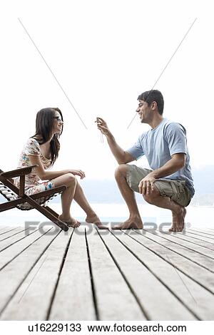 Stock Image - Young man photographing young woman on lounge chair. Fotosearch