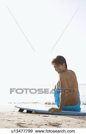 Young man sitting on surfboard on beach View Large Photo Image Stock Photo - Young man sitting on surfboard on beach. Fotosearch