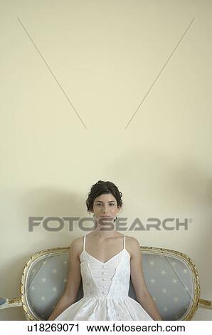 Stock Image - Young woman in white dress sitting on chair (portrait). Fotosearch