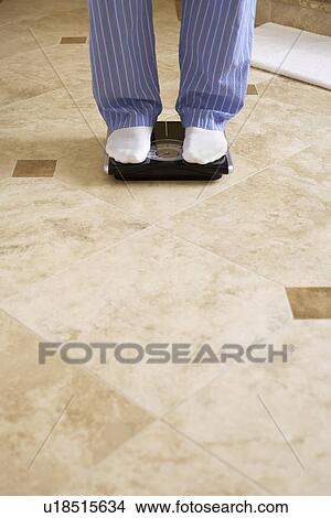 Picture - Mature man on bathroom scale (low section). Fotosearch