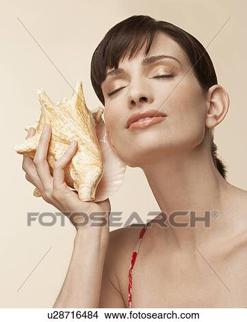 Mid adult woman holding conch shell to ear View Large Photo Image Picture - Mid adult woman holding conch shell to ear. Fotosearch