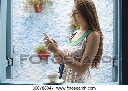Woman text messaging by window View Large Photo Image Stock Photo - Woman text messaging by window. Fotosearch
