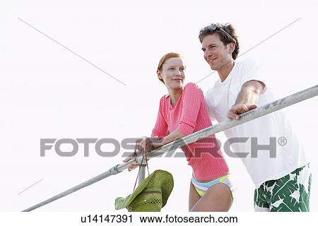 Stock Image - Young couple leaning against railings (low angle view). Fotosearch