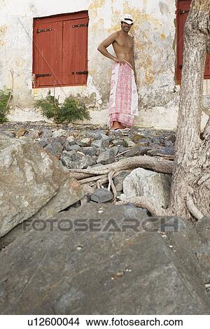 Young man in sarong and hat standing by old house View Large Photo Image Picture - Young man in sarong and hat standing by old house. Fotosearch