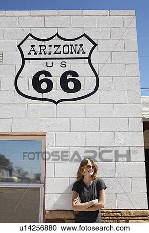 Stock Image - Young woman standing below Route 66 sign. Fotosearch