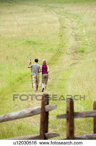 Stock Photograph - Couple walking in field near wooden gate. Fotosearch