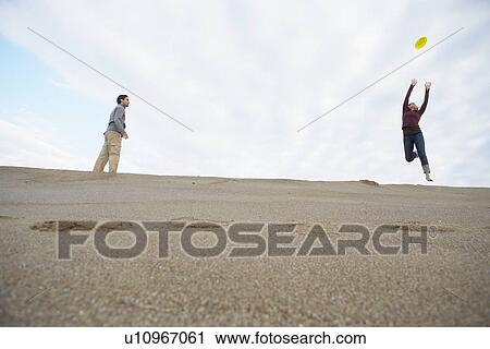 Stock Image - Man and woman throwing frisbee on beach (low angle view). Fotosearch