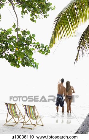Stock Image - Mid adult couple standing on beach and looking at view, St. John, US Virgin Islands, USA. Fotosearch