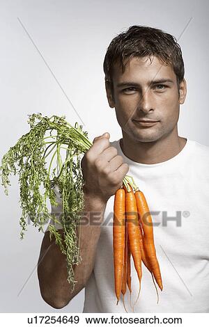 Stock Photo - Mid adult holding bunch of fresh carrots. Fotosearch