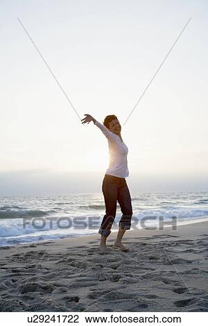 Stock Image - Mid adult woman running on beach. Fotosearch