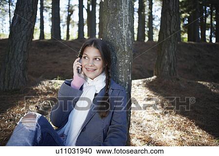 Stock Image - Teenage girl on cell phone in woods. Fotosearch