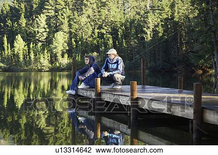 Stock Image - Two teenage boys sitting on jetty, Cape Town, South Africa. Fotosearch