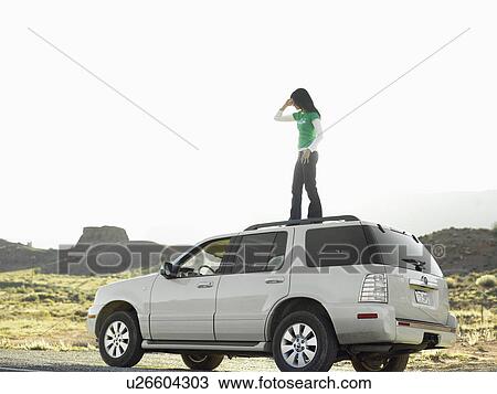 Stock Image - Woman using cell phone on roof of car, low angle view, Moab, Utah, USA. Fotosearch
