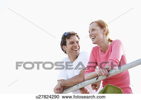 Stock Image - Young couple leaning against railings (low angle view). Fotosearch